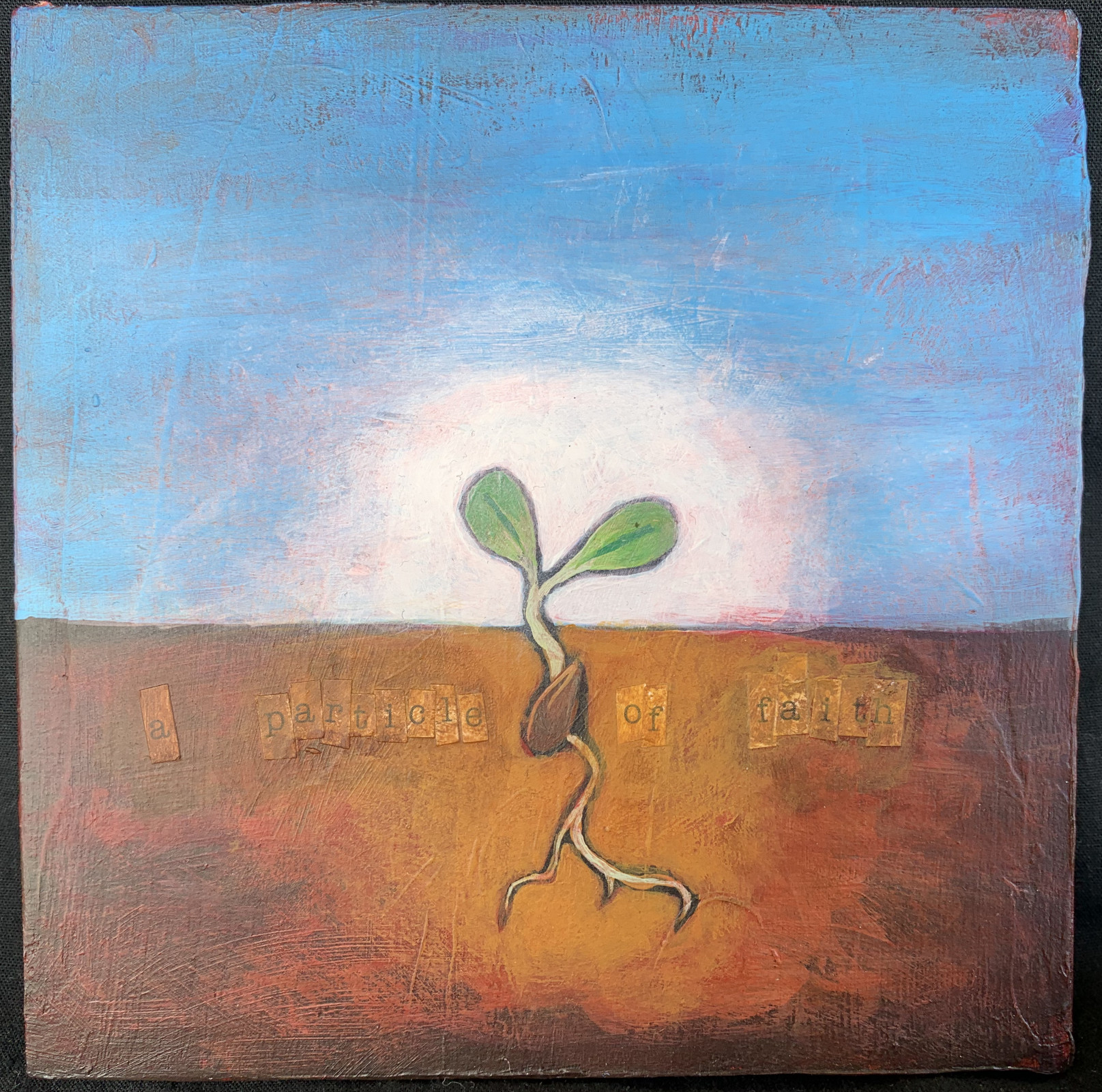 A square acrylic painting on board, featuring a germinating seed with two new leaves. The canvas is divided nearly in half, with blue sky above and earth below; the seed's roots are venturing into the soil. Around the roots, in cut-out letters, is the phrase "a particle of faith".